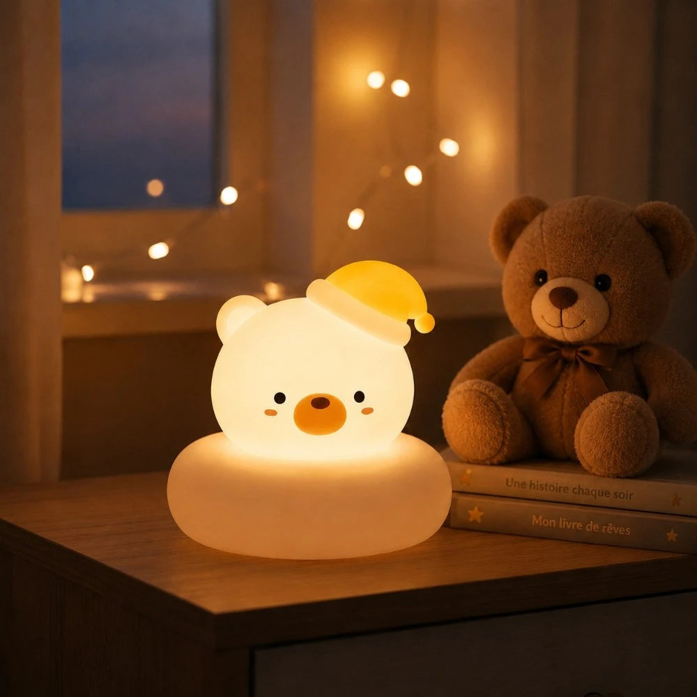 Veilleuse LED ours Bouba diffusant une lumière douce sur une table de chevet, aux côtés d'une peluche dans une chambre d'enfant.