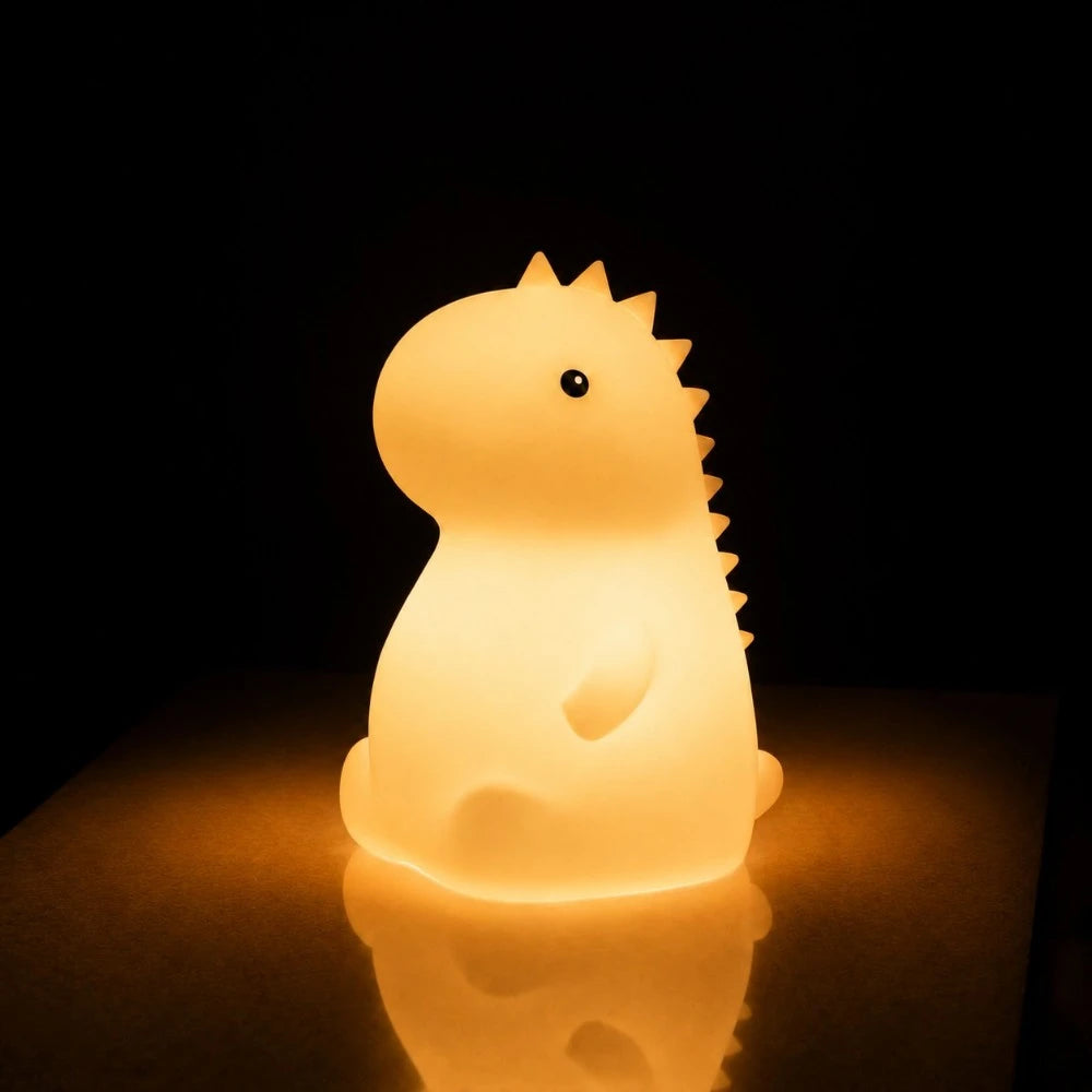 Veilleuse LED dinosaure Dyno allumée diffusant une lumière chaude avec reflet sur la table
