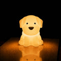 Veilleuse LED chiot Milo allumée diffusant une lumière chaude avec reflet sur la table