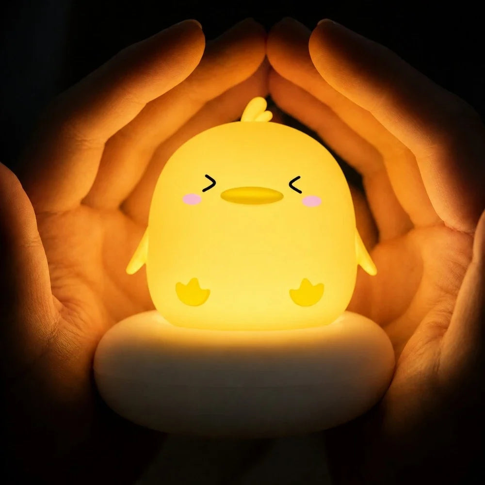 Veilleuse LED poussin Piou jaune allumée, diffusant une lumière chaude et entourée de deux mains.