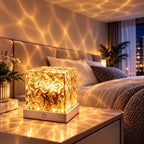 Veilleuse Aqua en lumière dorée sur une table de chevet, projetant des reflets d'eau chaleureux dans une chambre